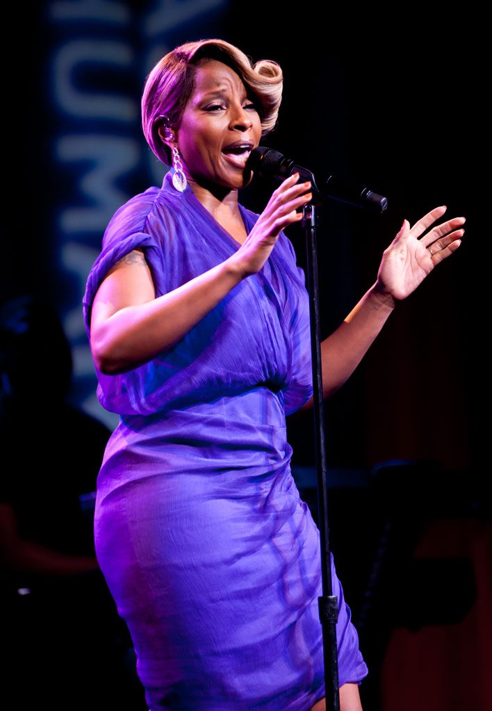 A woman in purple dress singing on stage.