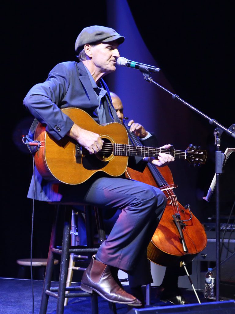 A man sitting on the floor playing an acoustic guitar.
