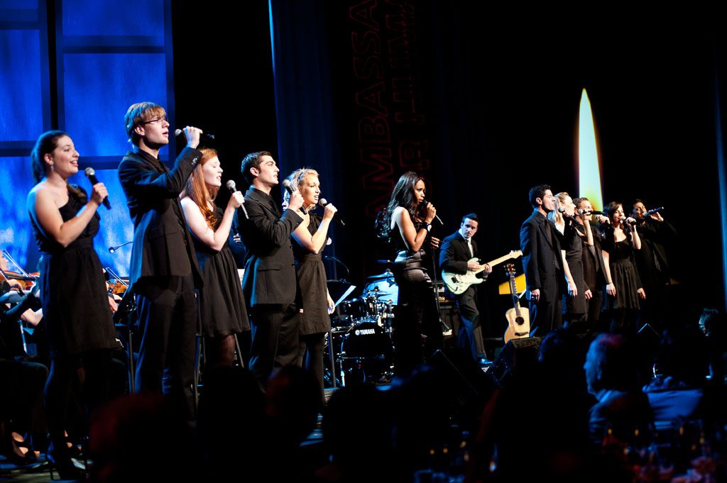 A group of people on stage singing and playing instruments.