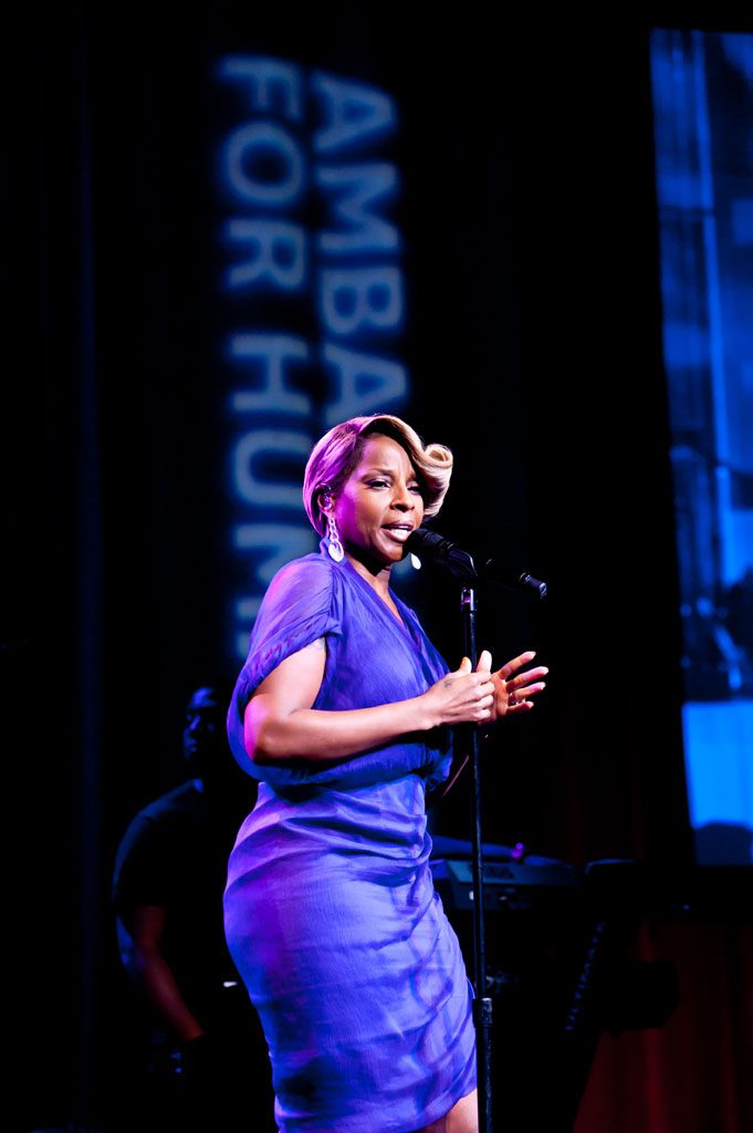 A woman in blue dress standing on stage with microphone.