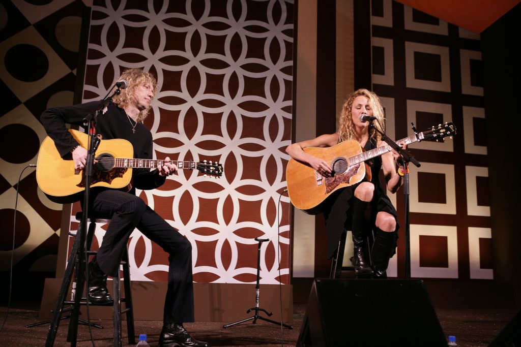 Two women are playing guitar and singing on stage.