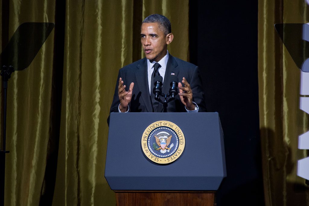 President obama speaking at a podium in front of a curtain.