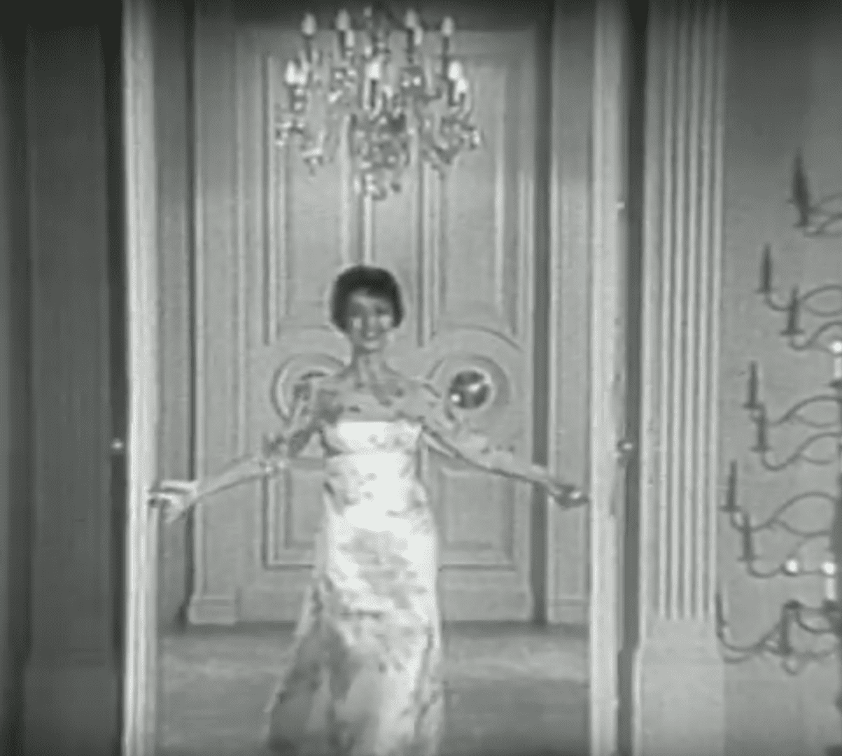 A woman in a white dress is standing by some doors